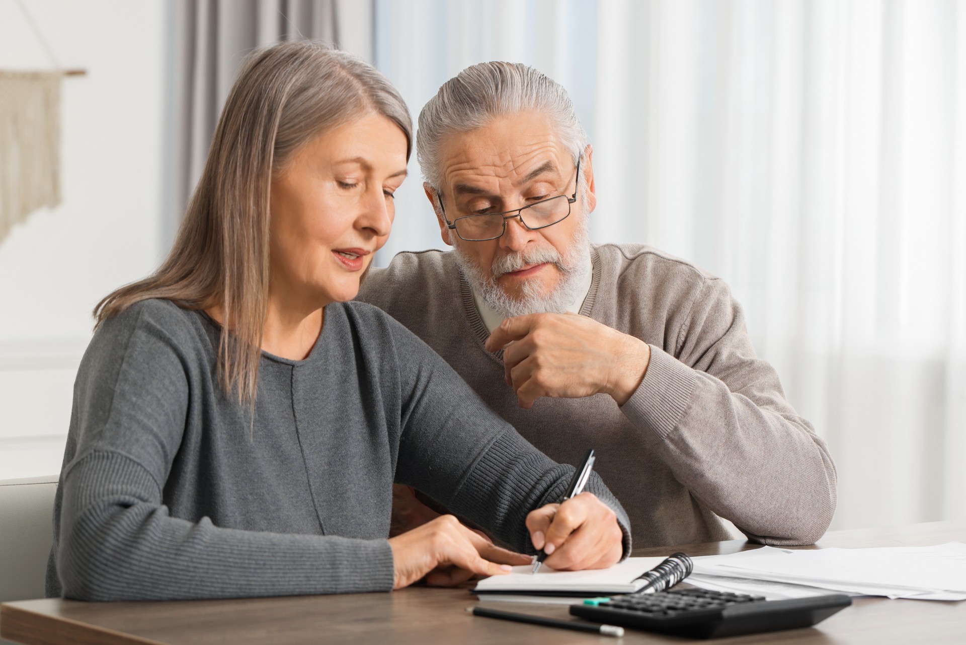 Elderly couple with papers discussing pension plan at wooden table indoors